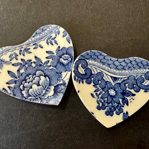 May include: Two heart-shaped ceramic dishes featuring a blue and white floral pattern. The left dish displays a large peony-like flower, while the right dish features a smaller floral cluster and intricate scrollwork along the upper edge.