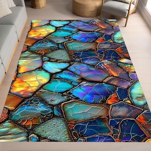 Könnte beinhalten: Ein rechteckiger Teppich mit einem abstrakten Design. Er zeigt ein Mosaikmuster aus unregelmäßigen, steinartigen Formen in Blau, Türkis, Orange und Lila. Das Design erzeugt ein farbenfrohes, strukturiertes Aussehen, das für die Inneneinrichtung geeignet ist.