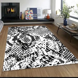Puede incluir: Una alfombra rectangular grande con un patrón de piel de serpiente en blanco y negro. La alfombra presenta un diseño repetido de escamas y texturas, creando una declaración gráfica audaz. La alfombra está colocada sobre un suelo de madera.