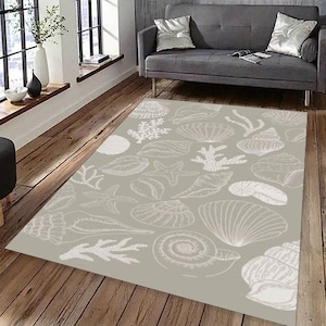 May include: A rectangular area rug with a light gray background and a white seashell pattern. The design includes various seashell illustrations, starfish, and coral. The rug is placed on a wooden floor, and a gray sofa is visible in the background.