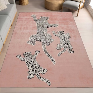 Puede incluir: Una alfombra rosa con un diseño de tres leopardos en una pose juguetona. Los leopardos son negros y blancos con un patrón de manchas.