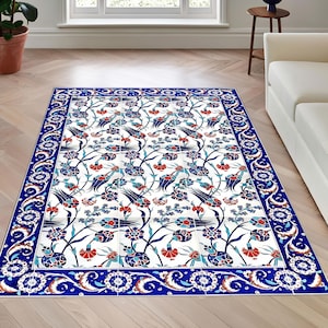 Può includere: Un tappeto bianco con un motivo floreale blu e rosso. Il tappeto ha un bordo blu con un design bianco e dorato.