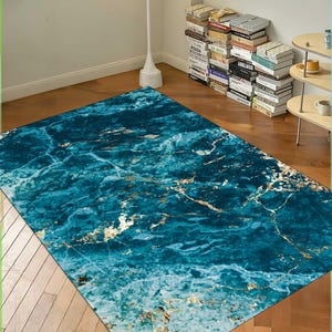 Op de afbeelding: Een blauw en gouden marmerpatroon tapijt met een modern ontwerp. Het tapijt heeft een lichtblauwe achtergrond met gouden aderen en swirls.