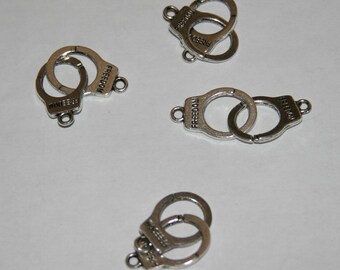 Pode incluir: Quatro pingentes de metal prateado em forma de algemas com a palavra "FREEDOM" gravada em cada um.