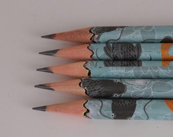 Könnte beinhalten: Nahaufnahme von fünf angespitzten Bleistiften. Die Bleistifte haben ein hellblaues Muster mit schwarzen und weißen Blumen- und Fischillustrationen. Die Bleistiftspitzen sind dunkelgrau und das Holz ist hellbraun.