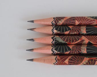 Könnte beinhalten: Nahaufnahme von fünf Bleistiften mit schwarzen Graphitspitzen. Die Bleistifte haben ein dekoratives Design mit einem Muster aus schwarzen und roten Fächern auf pfirsichfarbenem Hintergrund. Die Bleistifte sind in einer Reihe angeordnet.