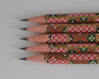 Könnte beinhalten: Nahaufnahme von fünf angespitzten Bleistiften mit rotem, goldenem und grünem Muster. Die Bleistifte sind parallel angeordnet, mit ihren Graphitspitzen nach links zeigend. Die Bleistifte haben ein dekoratives, geometrisches Muster.
