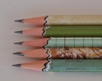 Könnte beinhalten: Nahaufnahme von fünf Bleistiften mit angespitzen Graphitspitzen. Die Bleistifte haben verschiedene Designs, darunter Grün, kariertes Papier und ein Vintage-Poststempelmuster. Jeder Bleistift hat ein rosa Radiergummiende mit dekorativem Rand.