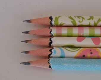 Könnte beinhalten: Nahaufnahme von fünf Bleistiften mit dekorativen Mustern. Die Bleistifte haben rosa Radiergummis und schwarze Graphitspitzen. Die Bleistiftzylinder weisen verschiedene Designs auf, darunter Blumen-, Karomuster und abstrakte Muster in Grün, Rosa, Blau und Orange.