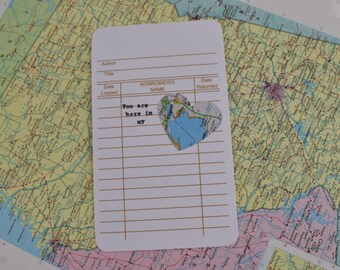 Könnte beinhalten: Eine weiße Karte mit einem linierten Rastermuster und dem Text "You are here in my" darauf gedruckt. Ein herzförmiges Stück Papier mit einer Karte einer Region ist an der Karte befestigt.