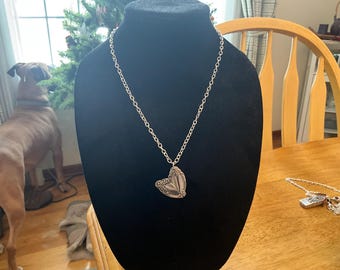 May include: Silver-toned necklace with a pendant shaped like a butterfly. The butterfly pendant is made from a repurposed utensil. The necklace is displayed on a black mannequin bust.