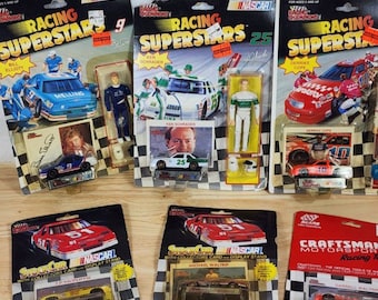 Op de afbeelding: Een verzameling van zes NASCAR Racing Superstar speelgoedautosets met de coureurs Bill Elliott, Ken Schrader en Derrike Cope. Elke set bevat een die-cast auto, een coureurfiguur en een verzamelaarskaart. De auto's zijn in verschillende kleuren, waaronder rood, wit, blauw en zwart.