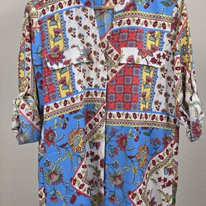 Op de afbeelding: Een overhemd met lange mouwen en knoopsluiting, voorzien van een levendig patchworkpatroon met blauwe, rode, gele en witte bloemen- en geometrische ontwerpen. Het overhemd heeft een opstaande kraag, twee borstzakken en oprolbare mouwen met Calvin Klein label.