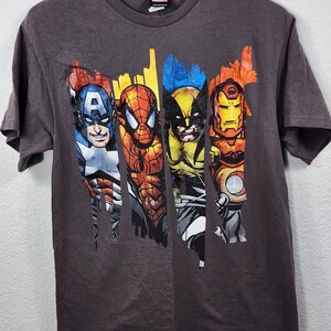 May include: A charcoal gray Marvel t-shirt featuring Captain America, Spider-Man, Wolverine, and Iron Man. The graphic design has a distressed, comic book style. The Marvel logo is visible at the top.