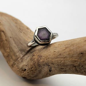 May include: A silver ring with a hexagonal purple gemstone set in a textured bezel.