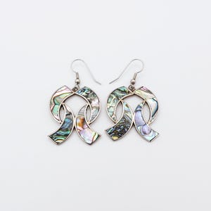 May include: A pair of silver earrings with a ribbon design. The earrings feature iridescent abalone shell inlays, displaying green, blue, and purple tones. The earrings have a hook closure.
