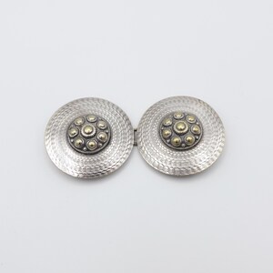 May include: A two-piece circular metal belt buckle featuring a textured silver-toned finish with a wavy pattern. Each circular component has a raised central medallion decorated with a cluster of small gold-toned spheres and beaded detailing.