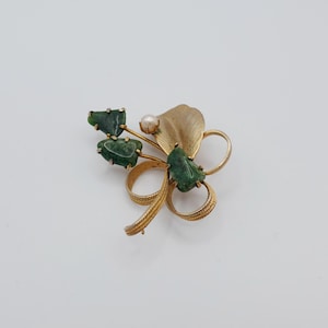 Puede incluir: Un broche de tono dorado con un diseño de flor de piedra verde y un acento de perla único.
