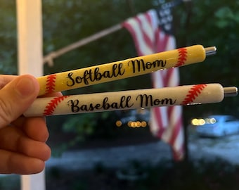 May include: Two baseball-themed pens, one yellow with red stitching and the text "Softball Mom", the other white with red stitching and the text "Baseball Mom".