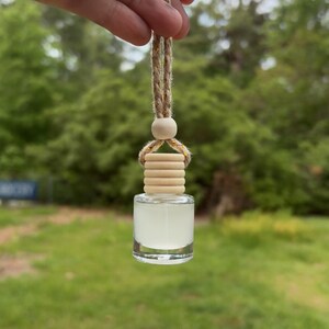 May include: A clear glass bottle with a wooden cap and a brown string hanging from it. The bottle is filled with a clear liquid and is hanging from a string.