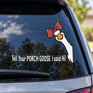 May include: A white vinyl decal on a car window featuring a cartoon goose with a red and white polka dot bow on its head. The goose is peeking from the side, and the text reads: Tell Your PORCH GOOSE I said Hi! in white capital letters.