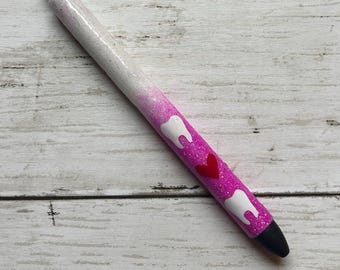 May include: A retractable pen featuring a glittery gradient finish that transitions from white at the top to bright pink at the bottom. The barrel is decorated with two white tooth icons and a single red heart icon positioned between them.
