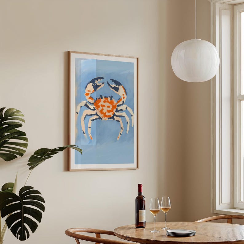 May include: A framed print of a blue, orange, and white crab on a light blue background. The crab is in the center of the print and is facing the viewer. The print is hanging on a light beige wall.