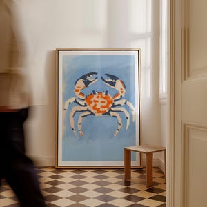 May include: A framed print of a stylized orange and blue crab on a light blue background. The print is hanging on a white wall in a room with a checkered floor.