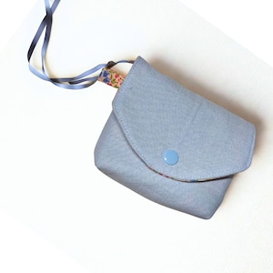 May include: A small, light blue fabric pouch with a flap closure and a light blue button. The pouch has a floral patterned lining and is attached to a blue ribbon. The pouch is likely used to carry small items.