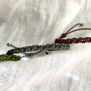Può includere: Tre braccialetti intrecciati con chiusure regolabili. I braccialetti sono verde, grigio e marrone.
