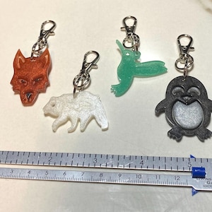 Puede incluir: Cinco llaveros con forma de animales con cierres plateados. Los llaveros incluyen un lobo rojo-naranja, un oso blanco, una foca verde y un pingüino negro y plateado. Una galga de costura y tejido de metal en la parte inferior, mide hasta 30 cm.