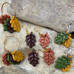 May include: Three pairs of earrings featuring autumn-themed leaf designs. Each pair features two leaves in different colors, including brown, green, orange, and yellow.