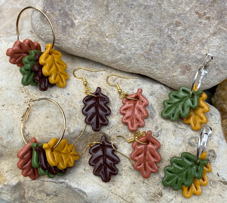 May include: Three pairs of earrings featuring autumn-themed leaf designs. Each pair features two leaves in different colors, including brown, green, orange, and yellow.