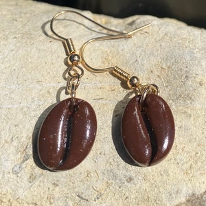 Puede incluir: Un par de pendientes de aro dorados con abalorios de granos de café marrones.