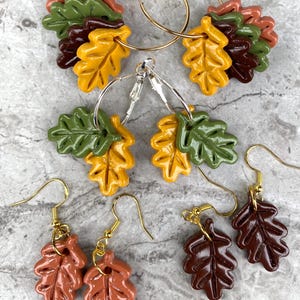 May include: Set of three pairs of autumn leaf earrings. The earrings are made of polymer clay and feature different colors and styles of leaves. The earrings are perfect for adding a touch of fall to any outfit.