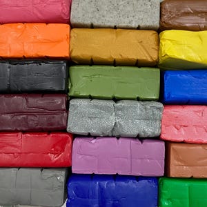 May include: A collection of 16 different colored polymer clay bars. The bars are arranged in a stack, with the colors alternating. The colors include pink, orange, black, burgundy, red, purple, gray, blue, green, brown, and yellow.
