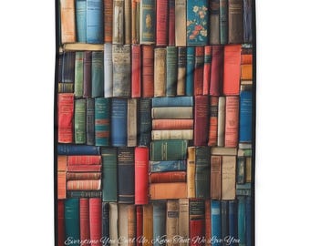 Pode incluir: Uma manta retangular com uma impressão de uma estante cheia de livros antigos. Os livros são de várias cores, incluindo vermelho, azul, verde e dourado. O texto "Everytime You Curl Up, Know That We Love You" está na parte inferior.