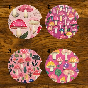 May include: Four round car coasters with mushroom designs. Each coaster features a different pattern of colorful mushrooms on a pink background. The designs include red, yellow, and white mushrooms with various patterns and sizes.