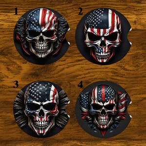 May include: Four black car coasters featuring skull designs with an American flag theme. Each coaster has a different skull design, with variations in the flag's placement and additional decorative elements. The coasters are round with a small notch.