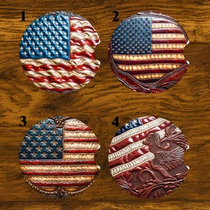 May include: Four car coasters with an American flag design. Each coaster is round with a cutout for easy removal. The coasters feature red, white, and blue colors, with stars and stripes.