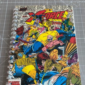 May include: A vintage comic book cover featuring the X-Men characters Wolverine, Cyclops, Storm, and others. The cover is a colorful illustration with a blue, yellow, and red color scheme. The title of the comic is "X-Force" and the issue number is 4. The cover also includes the Marvel Comics logo.