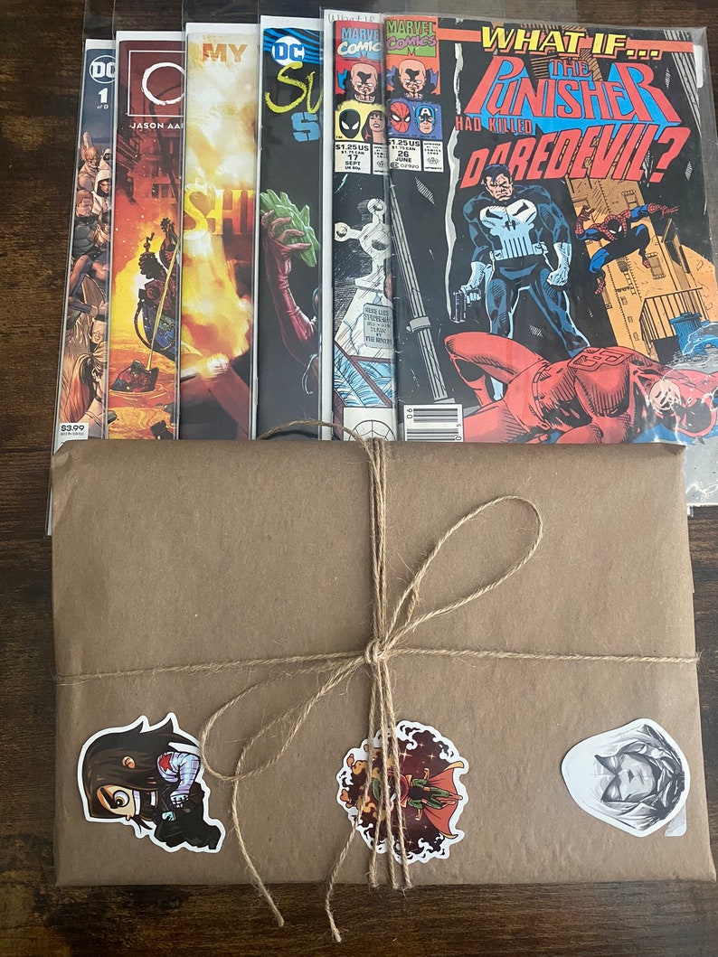 Pu&ograve; includere: Una pila di sei fumetti in buste protettive di plastica, inclusi titoli come What If The Punisher Had Killed Daredevil, dietro un pacchetto di carta marrone legato con spago e decorato con tre adesivi di personaggi.