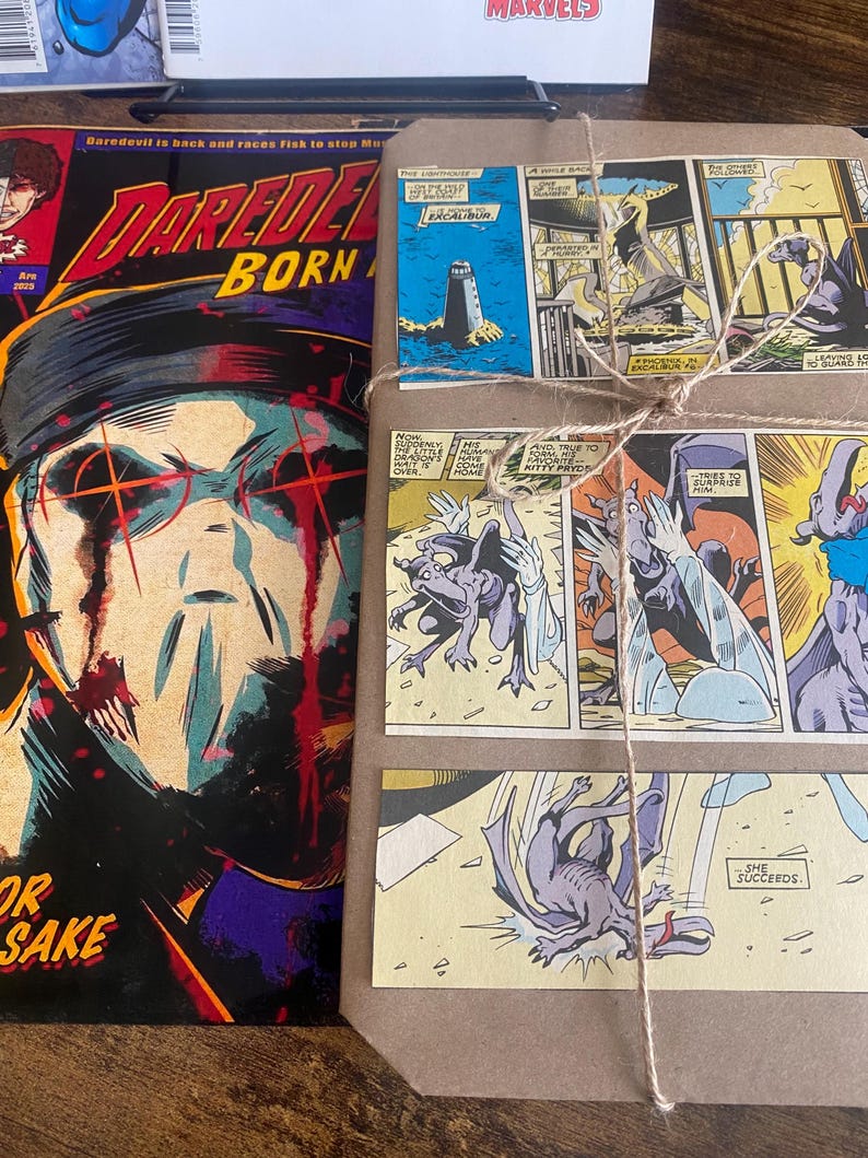 Pu&ograve; includere: Un fumetto Daredevil Born Again con un'illustrazione scura di una figura mascherata con occhi rossi, posizionato accanto a un pacchetto rettangolare avvolto in carta marrone e legato con spago, decorato con diversi pannelli di fumetti.