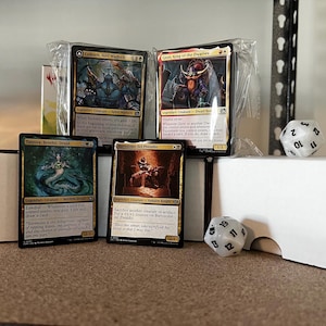 May include: A selection of Magic: The Gathering trading cards, depicting legendary creatures, alongside a white multi-sided die. The cards are in protective sleeves, displaying detailed artwork and text. The theme is fantasy and collectible card games.