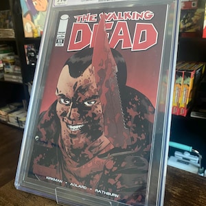 May include: A graded comic book of The Walking Dead #111, featuring a bloody image of a character with a knife. The comic book is graded 9.6 by CGC.