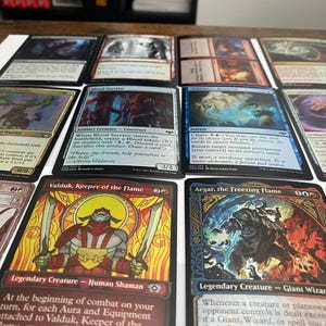 May include: A collection of Magic: The Gathering trading cards, featuring various card designs and artwork. The cards display text and illustrations, with a focus on fantasy themes and creatures. The cards are arranged on a white surface.