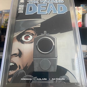 May include: A graded comic book of The Walking Dead #105, with a cover featuring a close-up of a man's face with a gun pointed at the viewer. The comic book is graded 9.6 by CGC.