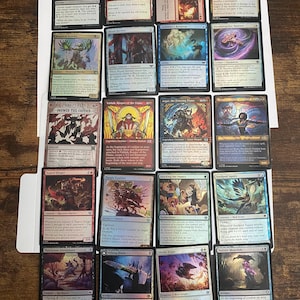May include: A collection of Magic: The Gathering trading cards, featuring various card designs with fantasy art and text. The cards are arranged on a white surface, showcasing a variety of colors and illustrations.