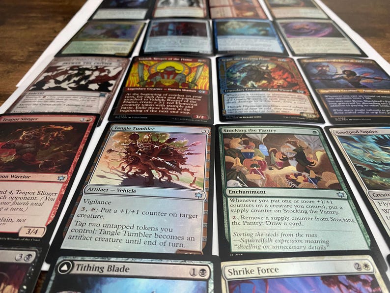 May include: A collection of Magic: The Gathering trading cards, featuring various card designs and artwork. The cards are arranged on a white surface, showcasing a variety of colors and illustrations. Some cards have text descriptions.