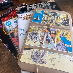 Pu&ograve; includere: Una pila di fumetti tra cui Moon Knight, Daredevil e The Amazing Spider-Man, con sopra un pacchetto avvolto in carta marrone e legato con dello spago. Il pacchetto presenta vignette a colori raffiguranti creature simili a gargoyle.